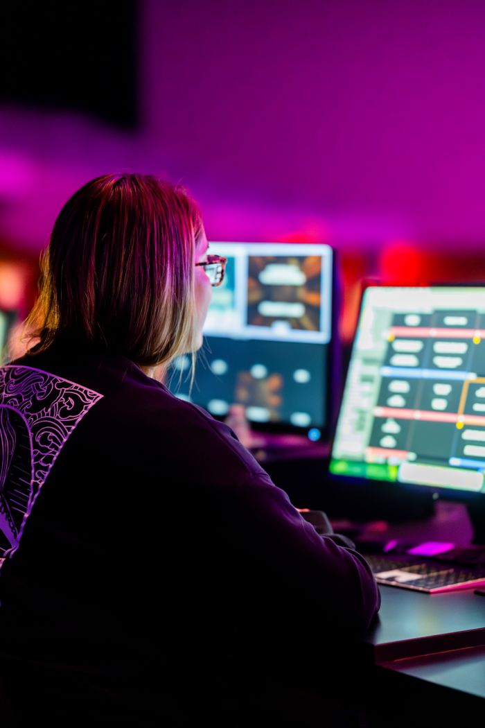 A female programmer is focused on multiple computer screens in a vibrant, colorful office environment.